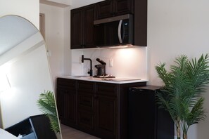 Una cocina compacta con armarios de madera oscura, un microondas integrado, un lavabo y un refrigerador pequeño.