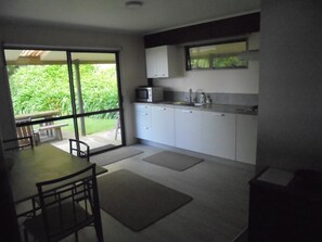 A modern kitchen with a dining area, large windows, and a view of greenery.