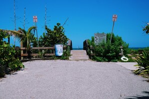 A beach entrance with no parking signs, a wooden walkway, and a signboard with information about sea turtles.