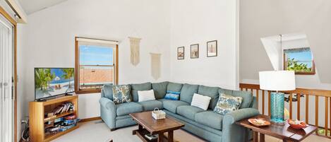 A living room with a sectional sofa, a television, a wooden coffee table, and a lamp.