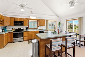 A modern kitchen with wooden cabinets, stainless steel appliances, and a large island with striped chairs. - White Dune: Dogs Allowed, Basketball Goal, Easy Beach Access (Avon)