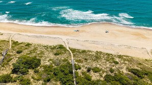 Vista aèria d'una platja amb un camí clar que condueix a la riba, envoltada d'una vegetació escassa.