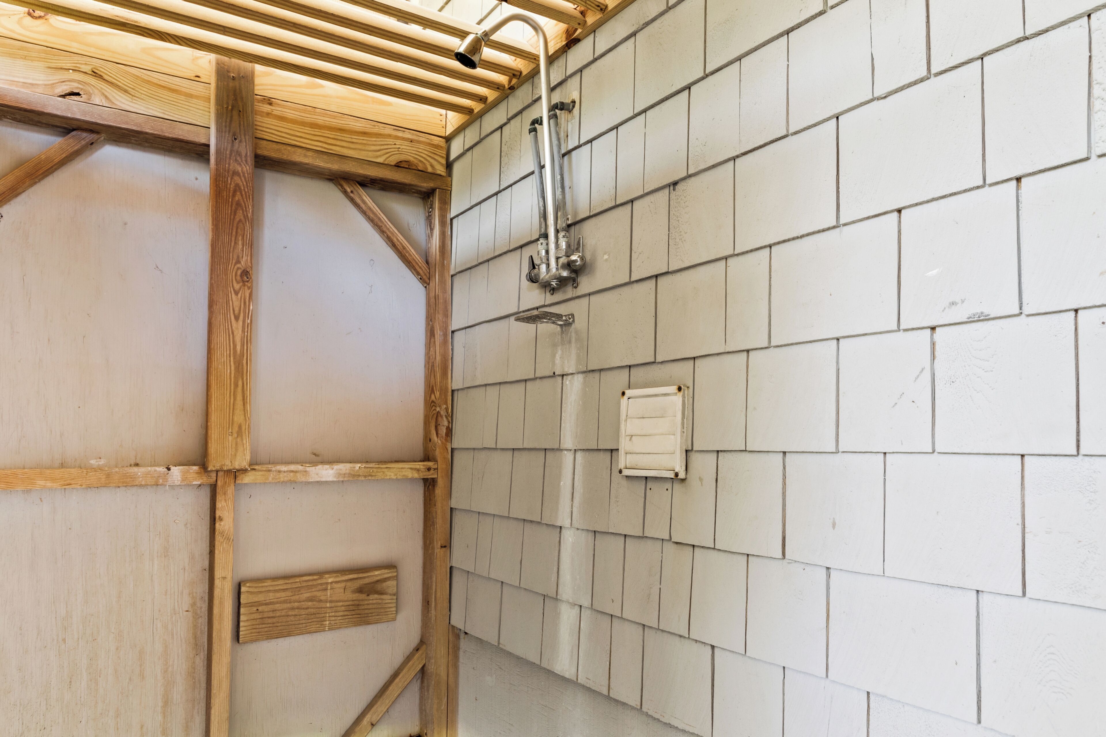 Een badkamer met houten balken, een betegelde muur en douchearmatuur.