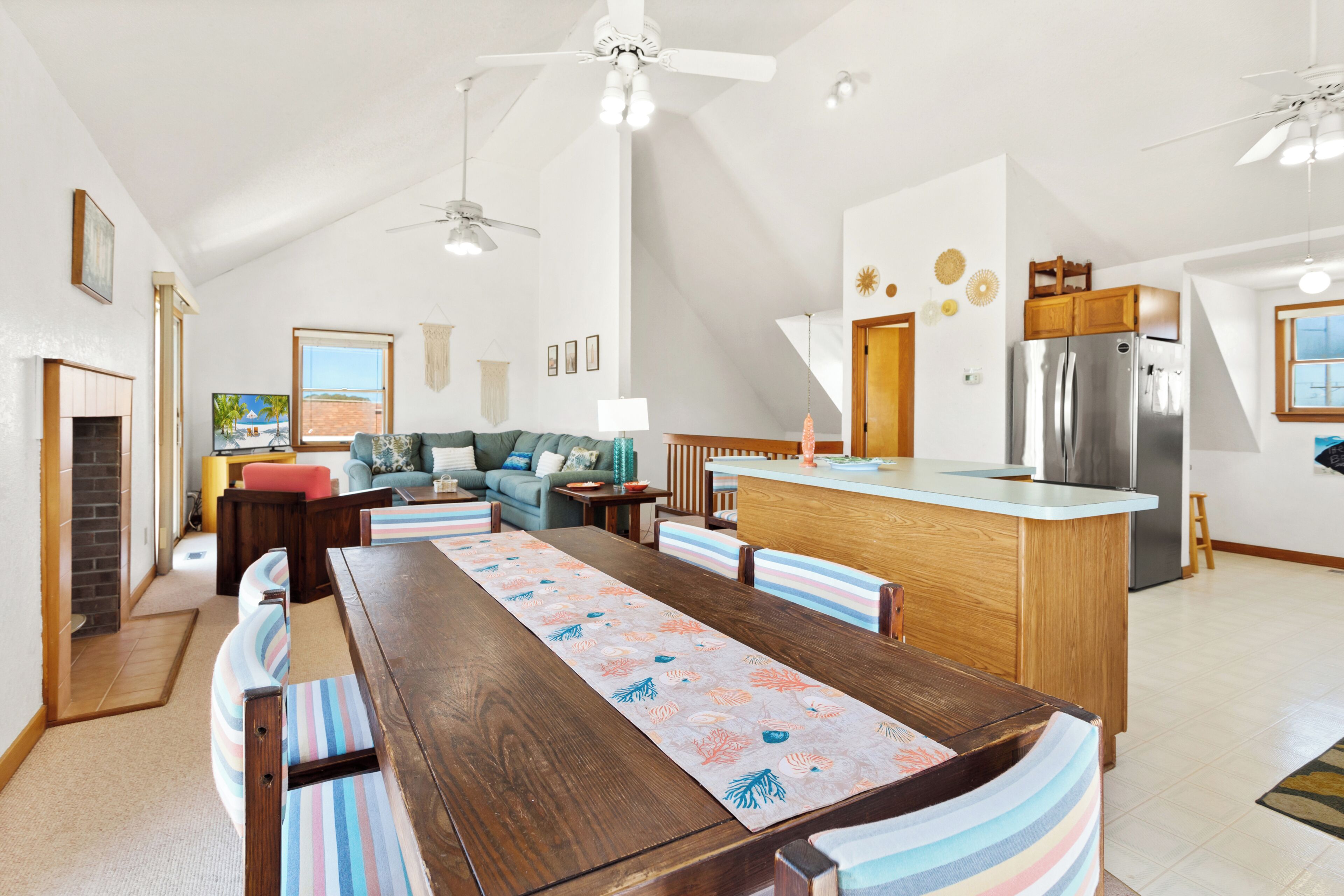 Una cocina amplia con una isla central, un comedor con bancos a rayas y una sala de estar con sofá y televisor.