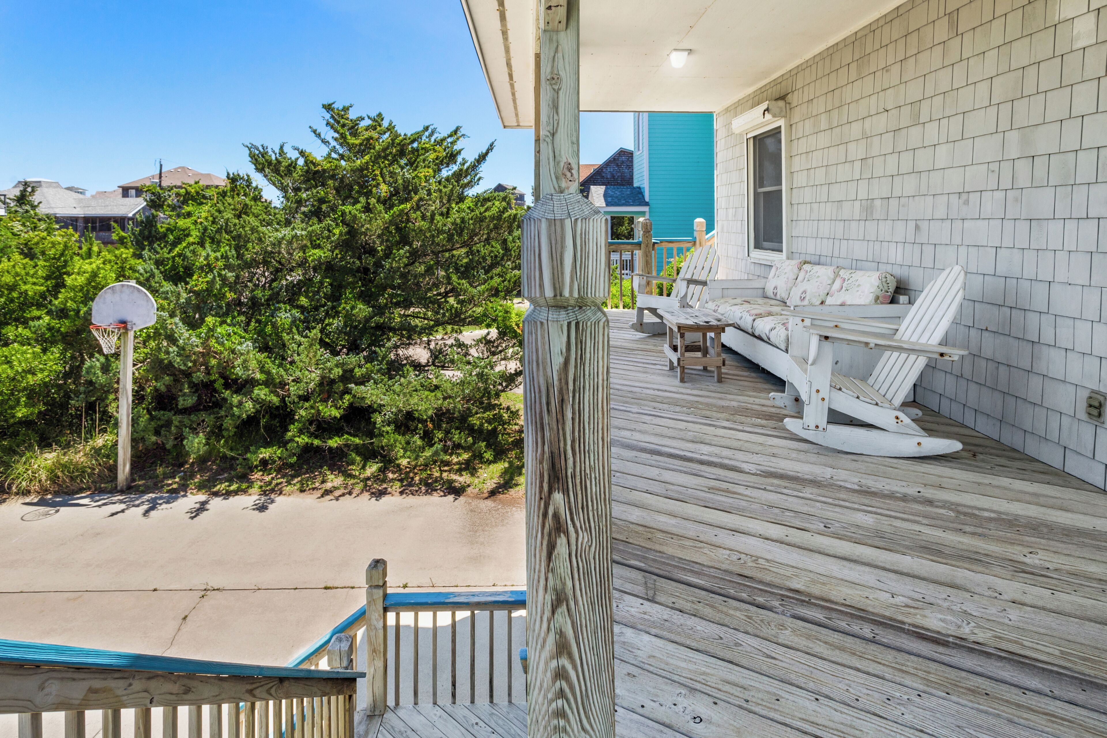 A wooden deck with a basketball hoop, a white outdoor seating area, and a house with a blue door.