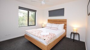 Un dormitorio con cama, ventilador de techo, ventana, lámpara de noche y televisor montado en la pared.