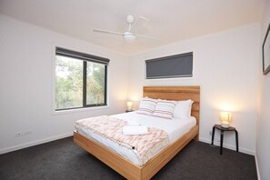 Une chambre à coucher comprenant un lit, un ventilateur de plafond, une fenêtre, une lampe de chevet et un téléviseur fixé au mur.