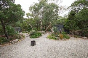 Une allée de gravier mène à un bâtiment entouré d’arbres et d’arbustes.