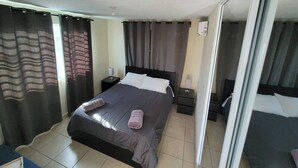 A bedroom with a bed, two bedside tables, a nightstand, a sliding glass door, and a window with curtains.