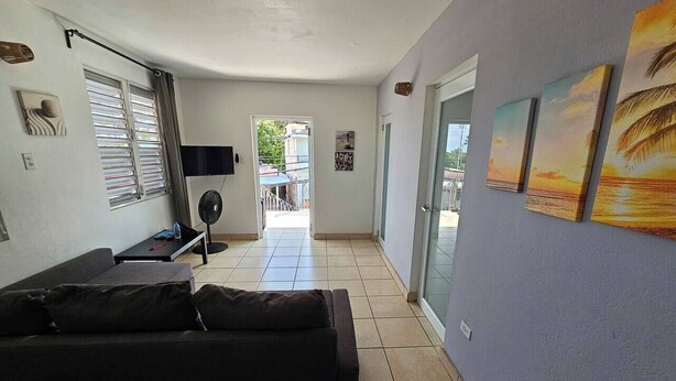 A living room with a sofa, a TV, a fan, and artwork on the walls.