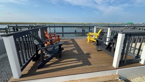 Een houten terras met buitenmeubels, een hekwerk en uitzicht op het water.