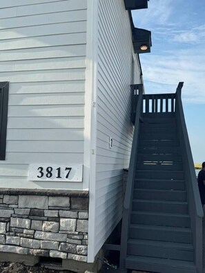 A house with a stone foundation, a number '3817' sign, and a wooden staircase leading up to the entrance. - Sunset-bay condo #2!   -2 BR/1 BA - 2nd floor (Brigantine)