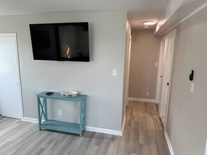 A hallway with a TV mounted on the wall, a teal console table with a bowl and a remote, and wooden flooring. - Sunset-bay condo #2!   -2 BR/1 BA - 2nd floor (Brigantine)