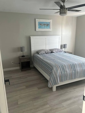 Ein Schlafzimmer mit einem Bett, Nachttischen, einem Deckenventilator und einem gerahmten Bild an der Wand.