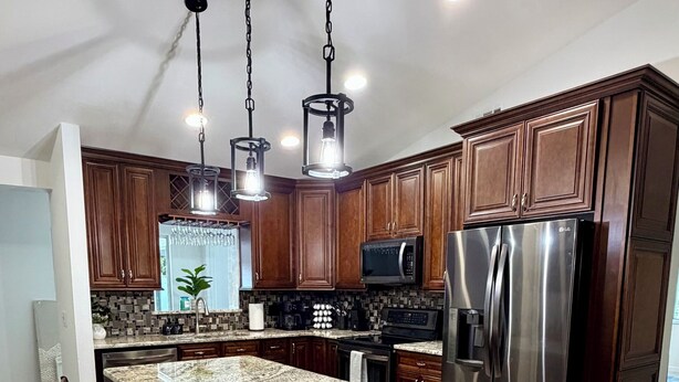 A modern kitchen with wooden cabinets, stainless steel appliances, and a granite island. - New - Sleeps 10 Private Pool and Fenced Yard (Orlando)
