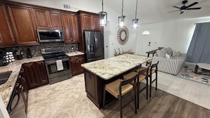 A kitchen with wooden cabinets, a stainless steel refrigerator, a microwave, and a granite countertop island with bar stools. - New - Sleeps 10 Private Pool and Fenced Yard (Orlando)