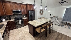 Eine Küche mit Holzschränken, einem Edelstahlkühlschrank, einer Mikrowelle und einer Kücheninsel mit Granitplatte und Barhocker.