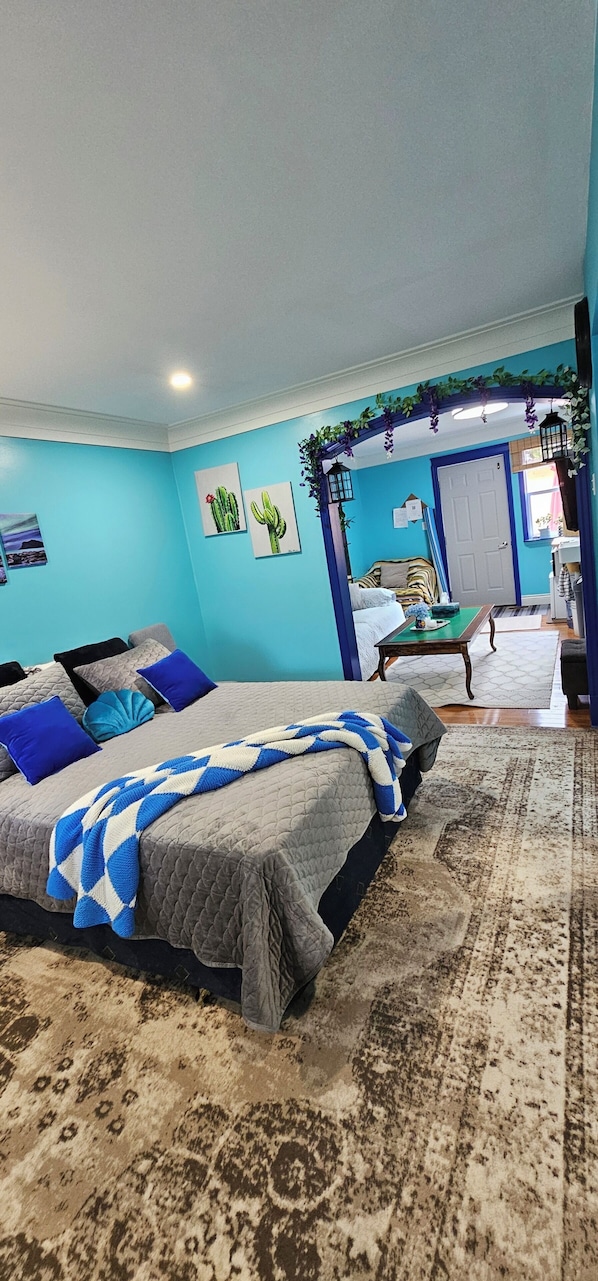 A bedroom with a bed, a nightstand, a dresser, and a door leading to another room.