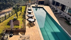 A rooftop pool with lounge chairs and tables, surrounded by a view of distant hills.