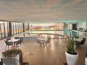 A spacious indoor area with a pool, seating arrangements, and large windows offering a view of the outdoors.