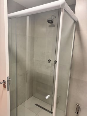 A glass-enclosed shower stall with a handheld showerhead, a control panel, and a towel dispenser.