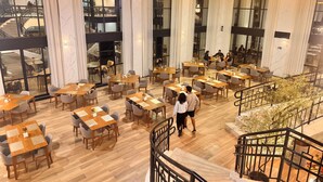 A modern dining area with multiple tables and chairs, large windows, and a staircase.
