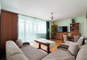 Ein Wohnzimmer mit einer Sofagarnitur, einem Holzschrank, einem Fernseher und einem Essbereich.
