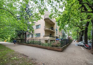 Ein mehrstöckiges Wohngebäude mit Balkon, gepflastertem Weg und einer Einfriedung.