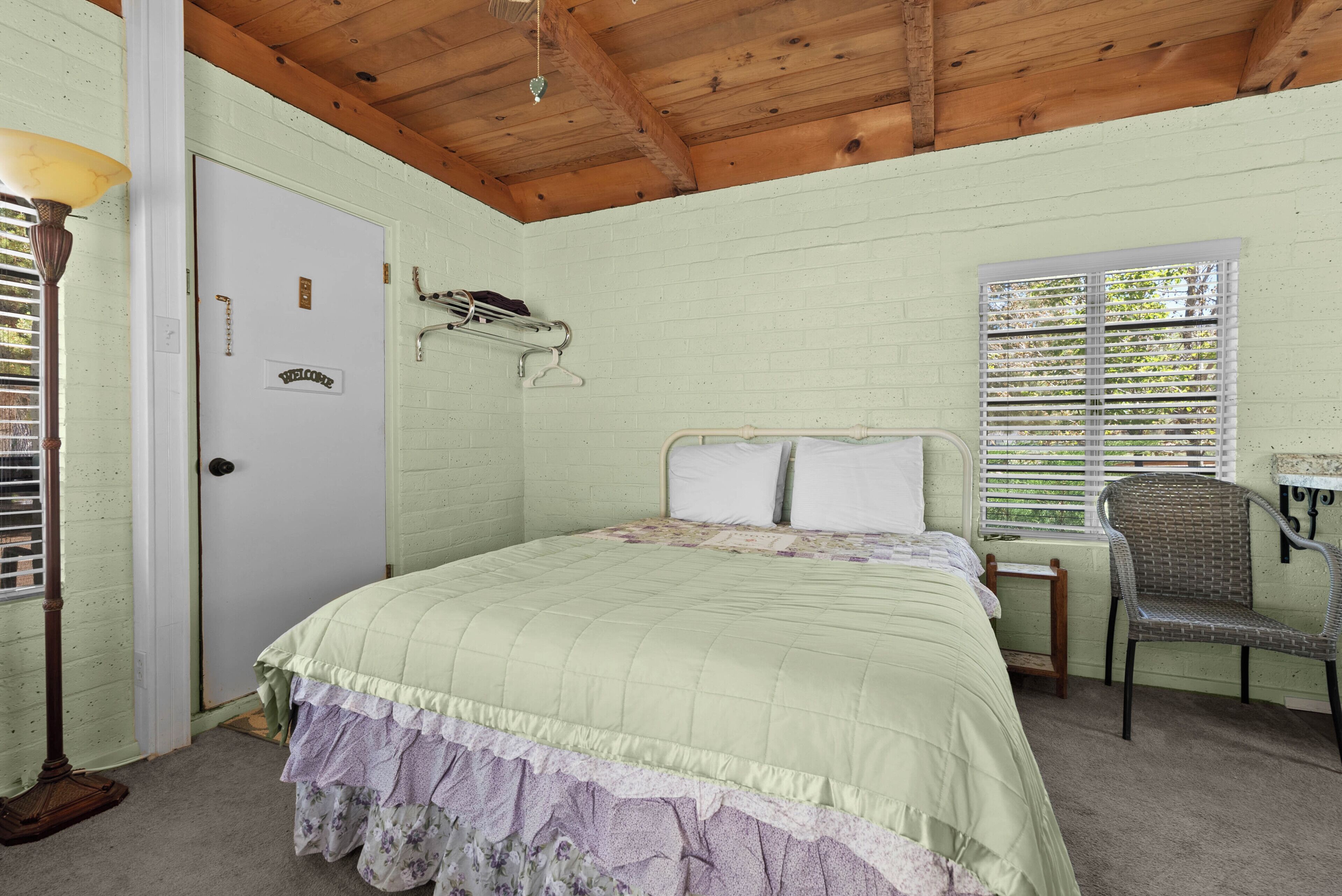 Une chambre à coucher avec un lit, une chaise, une lampe, une porte et une fenêtre avec des stores.