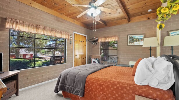 A bedroom with a large window, a ceiling fan, a bed with a patterned bedspread, and a wooden headboard. - Sierra cabin for two with a cheerful retro kitchen, minutes from Topaz Lake (Coleville)