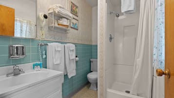 A bathroom with a sink, mirror, towel rack, shower, toilet, and a wall-mounted hairdryer.