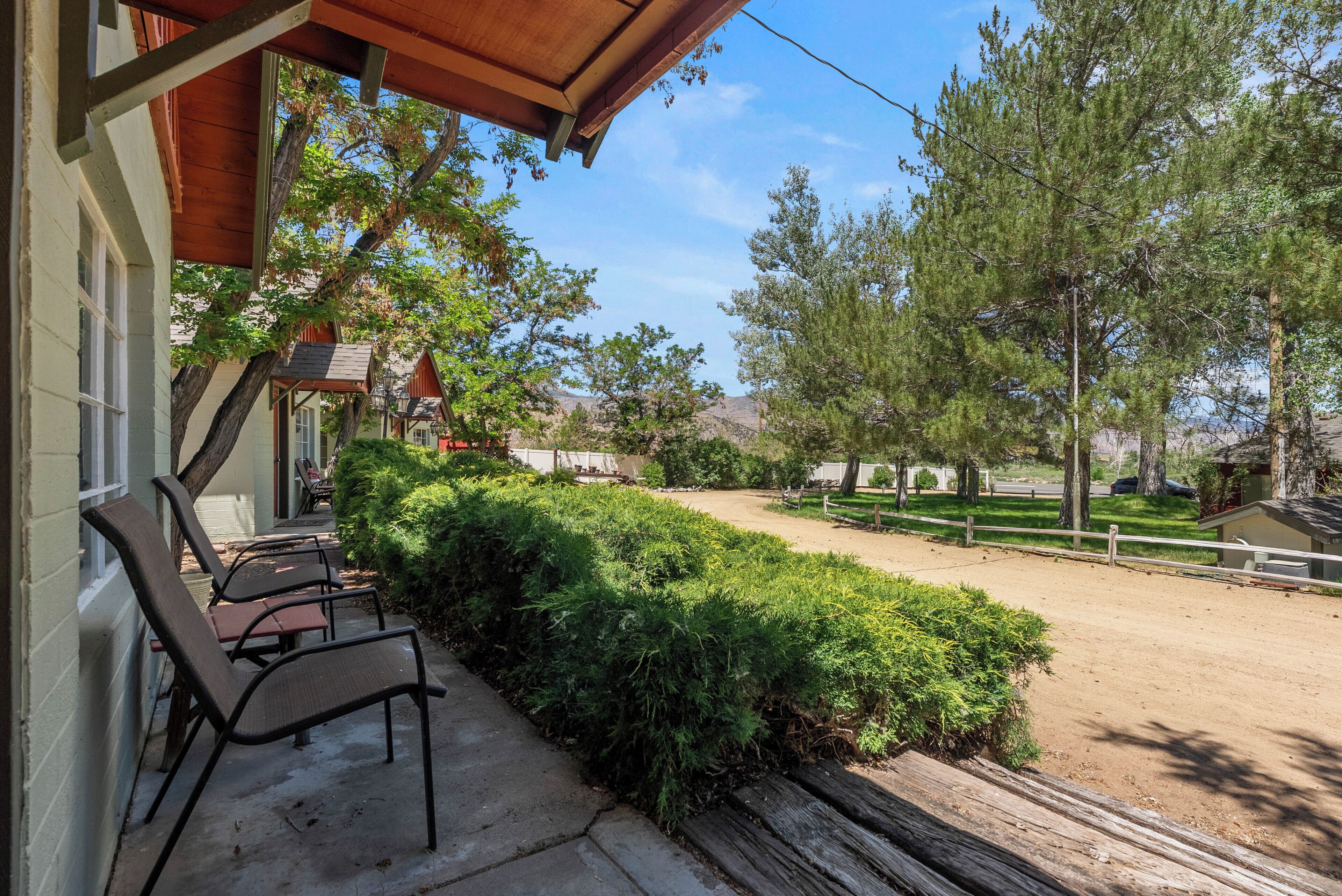 A covered outdoor seating area with chairs, a wooden fence, and a well-maintained lawn.