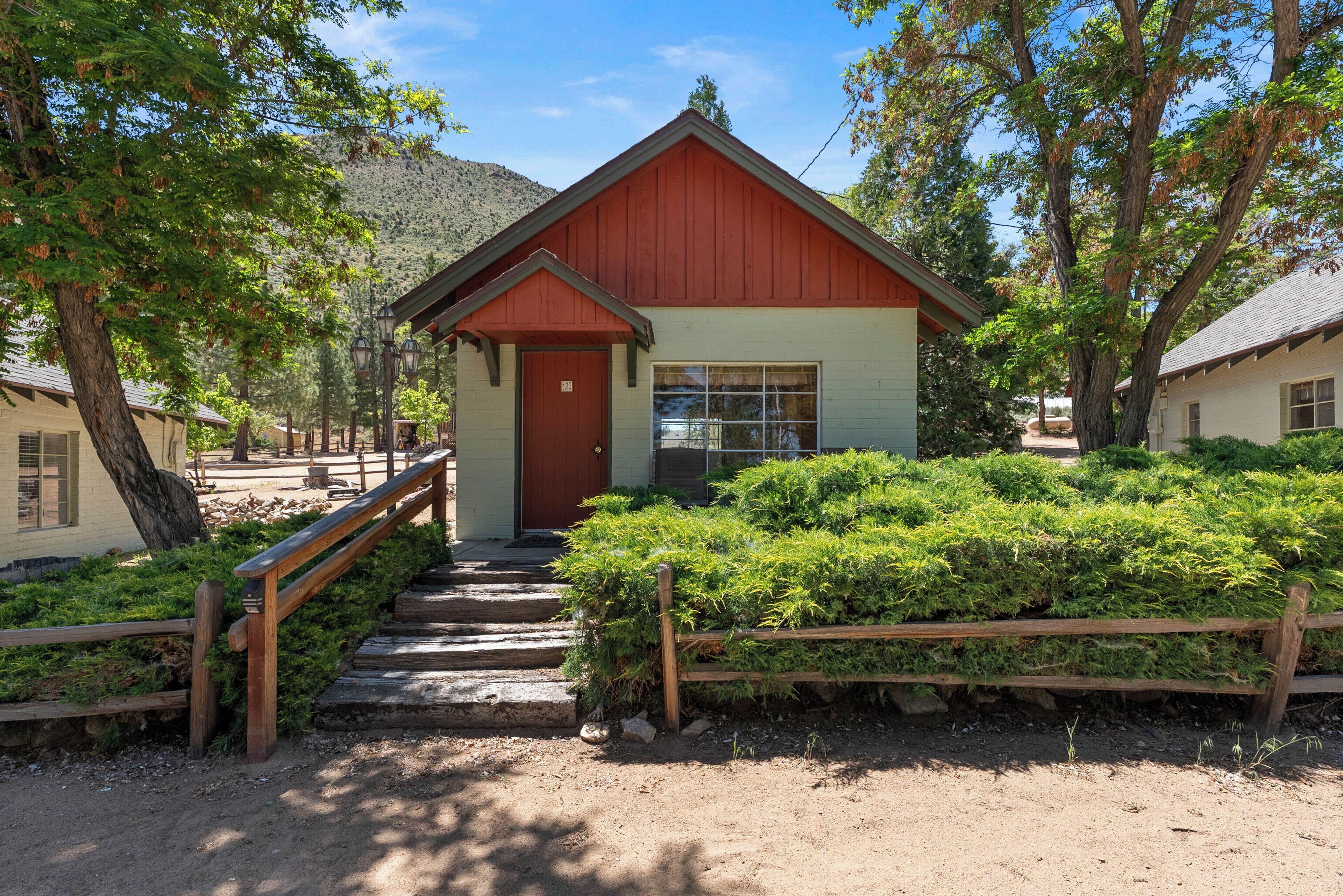 Un petit bâtiment avec un toit rouge et une seule porte, entouré de verdure et d’une clôture en bois.