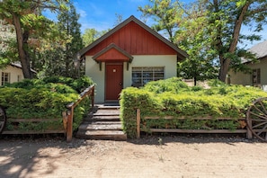 A small building with a red door and a window, surrounded by greenery and a wooden fence. - Comfortable cabin for two with full kitchen and a freshly updated bathroom, near Topaz Lake (Coleville)