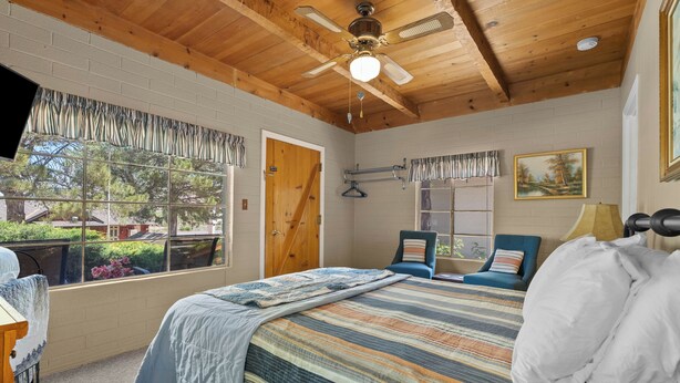 Un dormitori amb un llit, un ventilador de sostre, una finestra amb cortines, una porta i un quadre a la paret.
