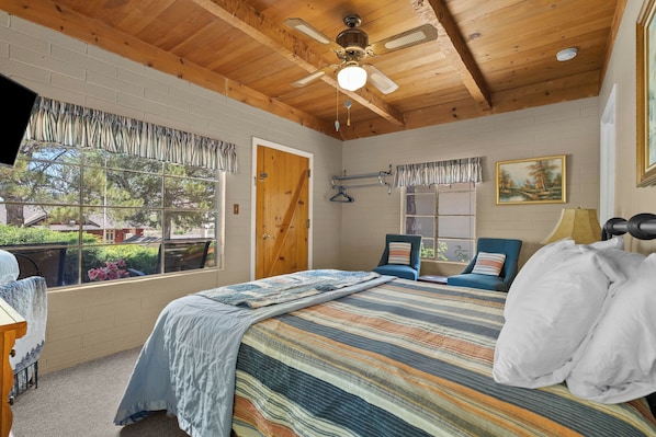 A bedroom with a bed, a ceiling fan, a window with curtains, a door, and a painting on the wall. - Comfortable cabin for two with full kitchen and a freshly updated bathroom, near Topaz Lake (Coleville)