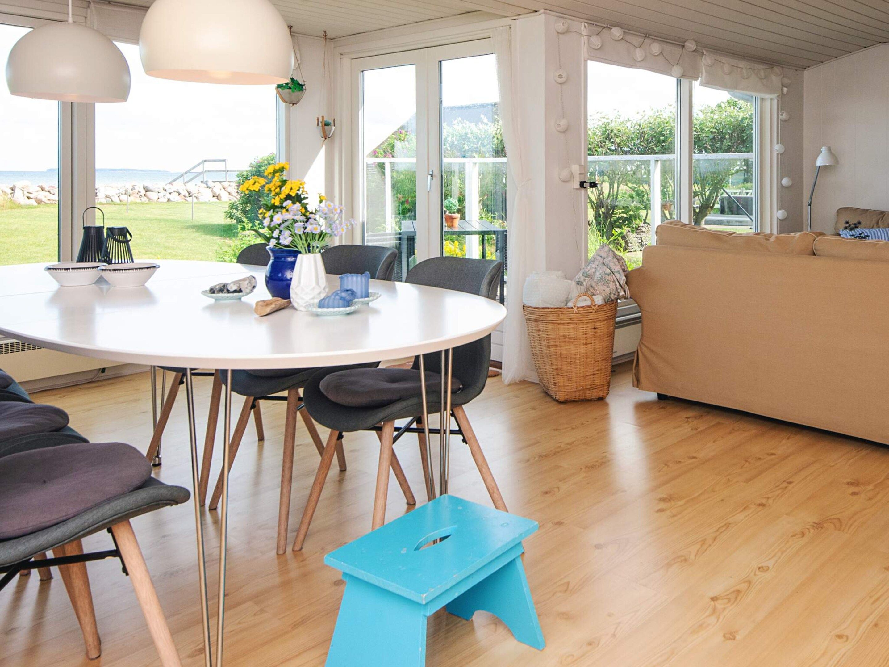 Ein Essbereich mit einem runden Tisch, Stühlen und einem blauen Hocker. Im Hintergrund befindet sich ein Korbwäscher und eine Couch.