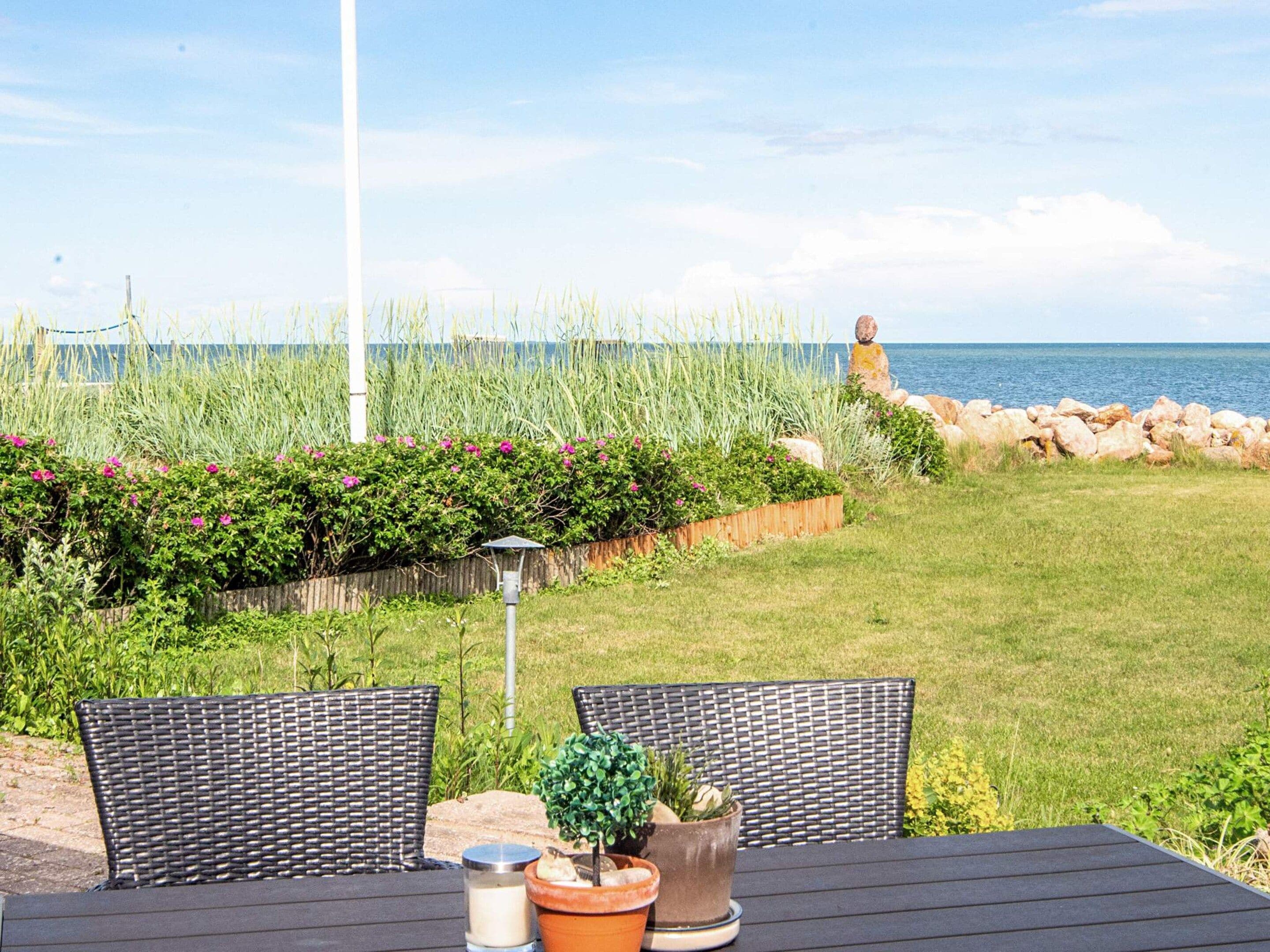 An outdoor seating area with wicker chairs and a table, overlooking a grassy area with a view of the sea.