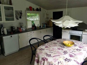 A kitchen with white cabinets, a dining table with a floral tablecloth, and a yellow bowl on the table. - 4 Star Holiday Home in Frederiksvaerk (Frederiksvaerk)