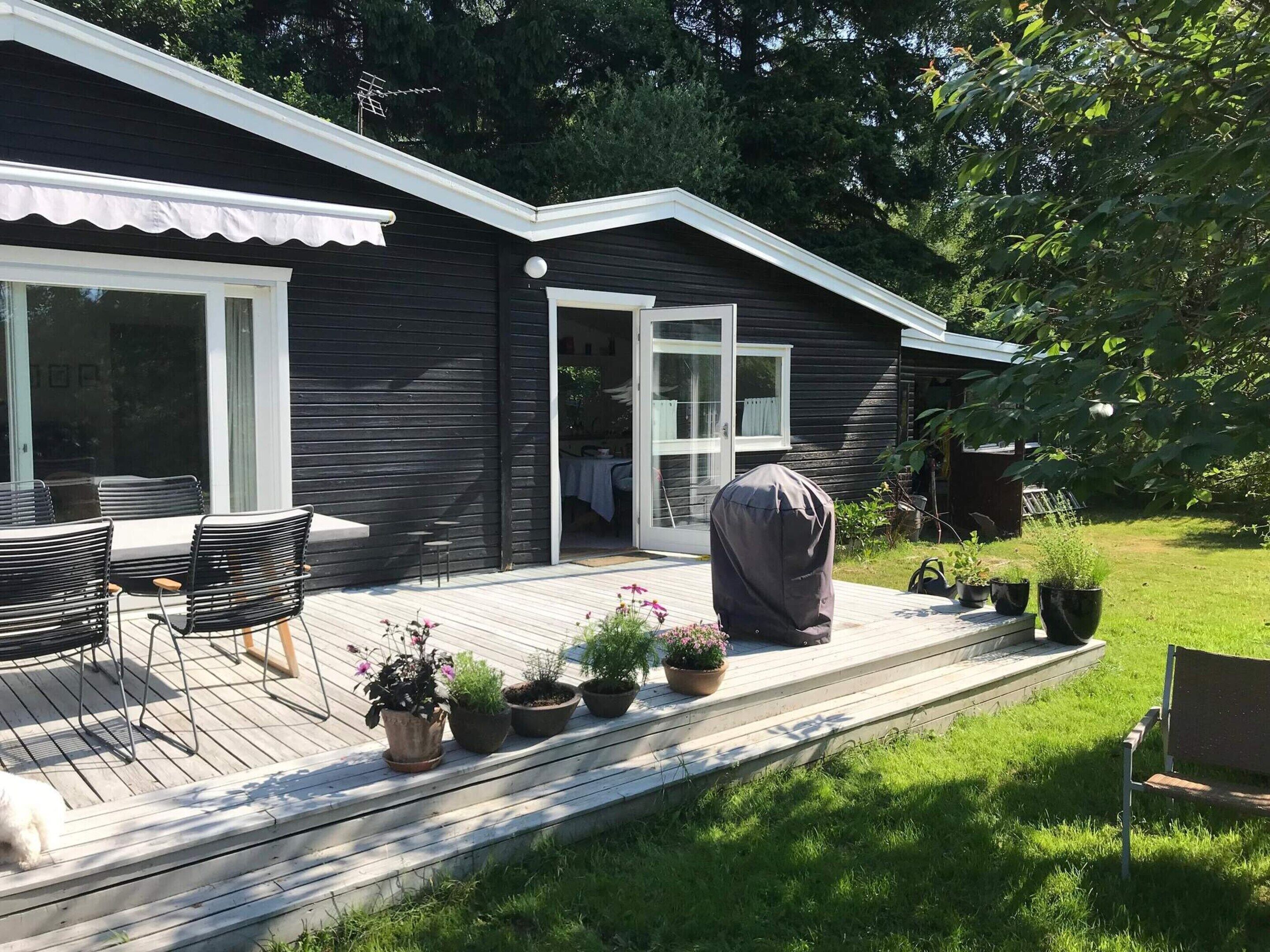 A modern house with a deck, outdoor seating, and potted plants.
