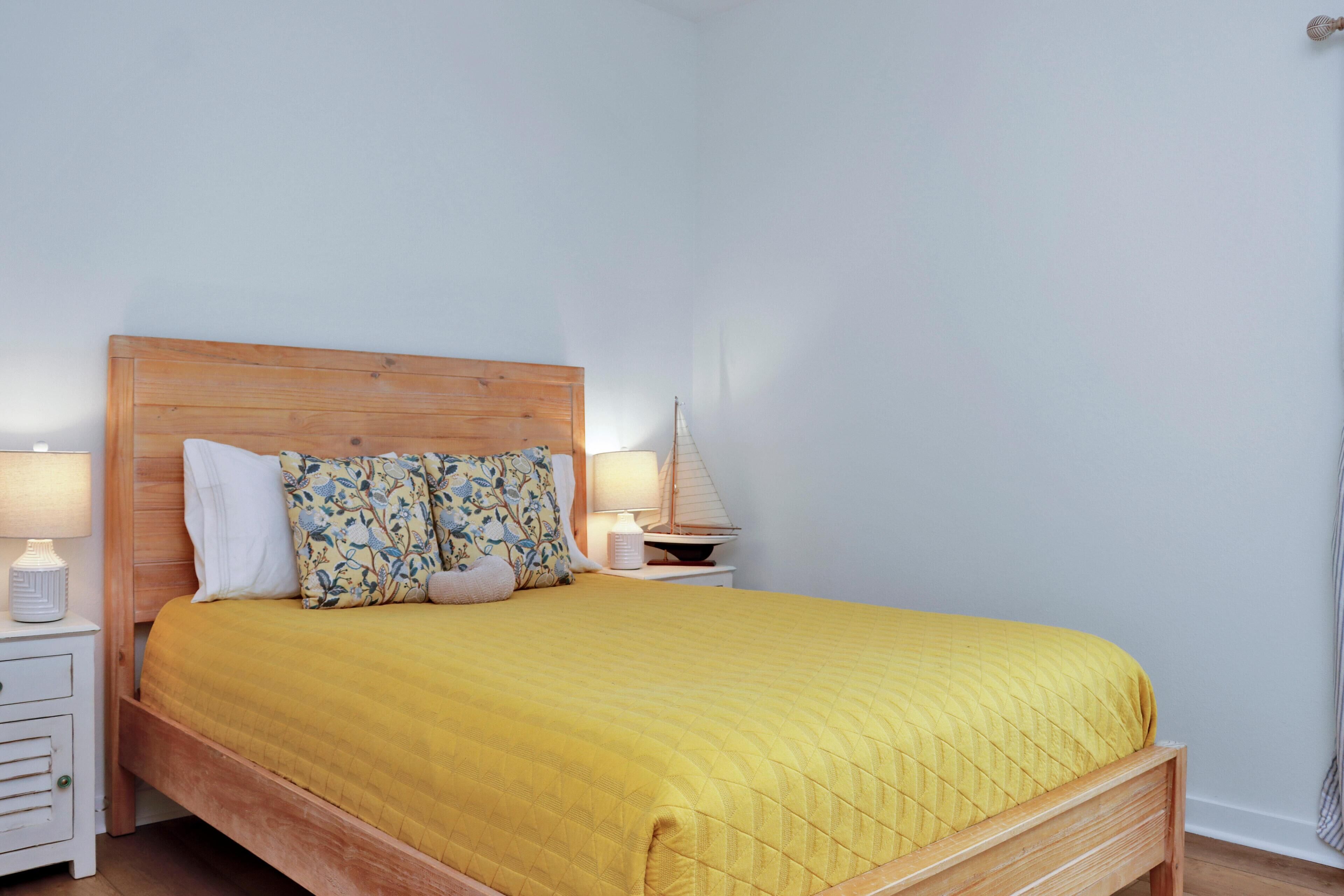 A bed with a wooden headboard, a yellow quilt, and two bedside lamps.