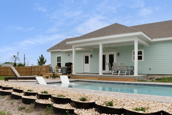 Une maison avec une piscine, un patio couvert et du mobilier d’extérieur.