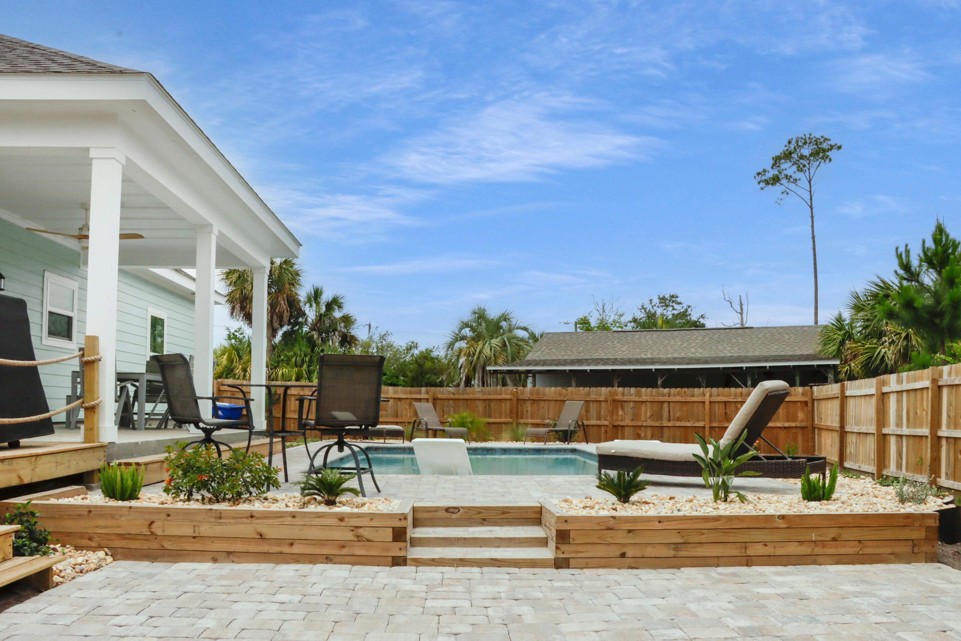 Patio con piscina, terraza de madera y mobiliario exterior.