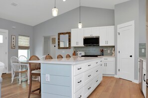 Une cuisine moderne avec des meubles blancs, un grand îlot central et des luminaires suspendus.