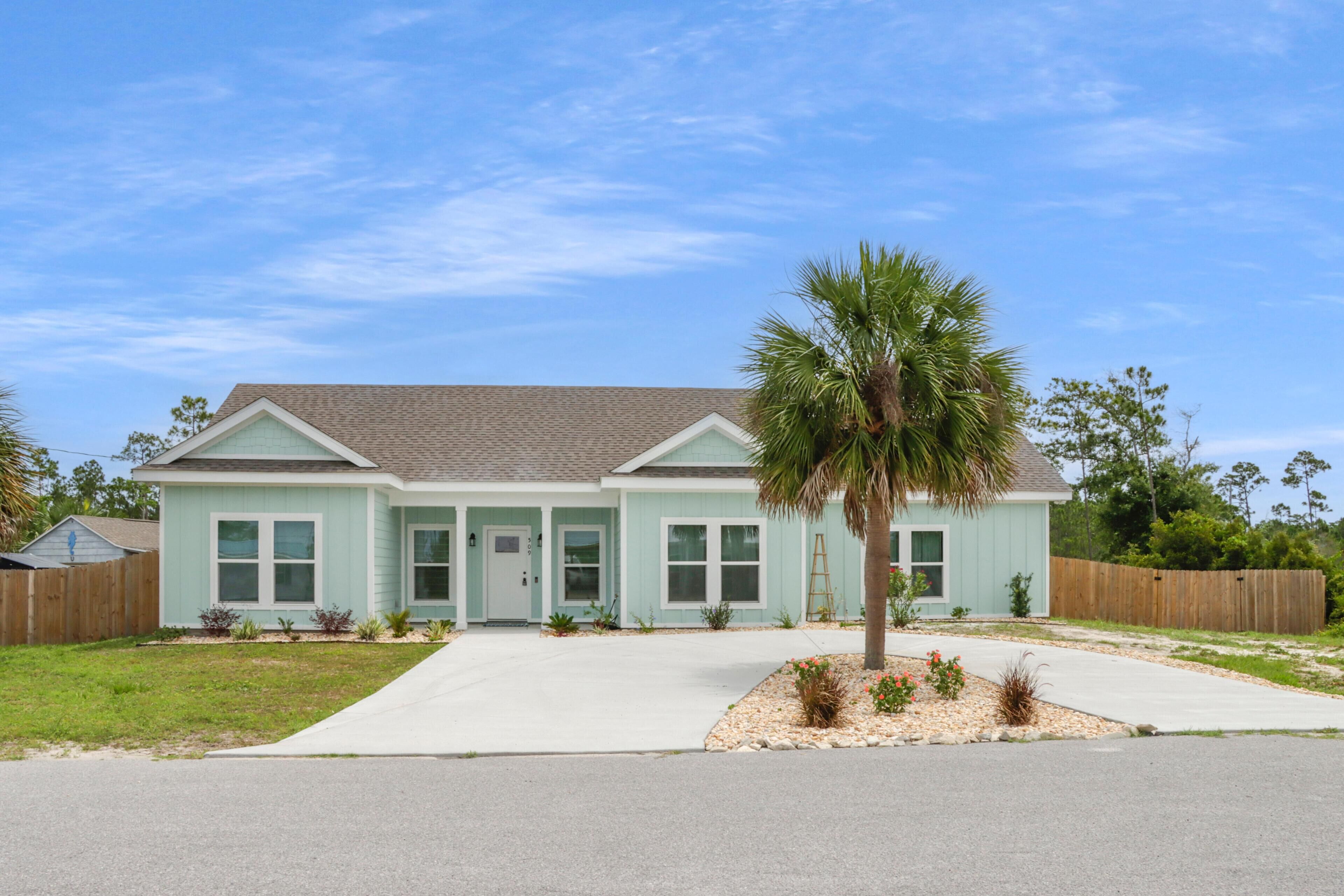 A single-story house with a front porch, a palm tree, and a wooden fence.