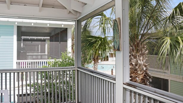 A covered balcony with a railing, a view of a swimming pool, and palm trees. - Barefoot Cottage B28 (Port St. Joe)