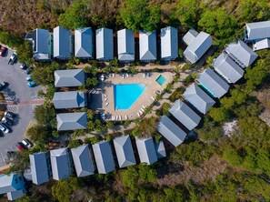 Ett flygbildsbild av ett semesterområde med flera byggnader i bungalowstil, placerade runt en central pool.