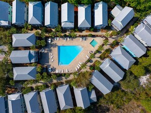Ett flygbildsbild av ett semesterområde med flera byggnader, en central pool och palmer runt omkring.