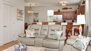 A modern living room with a gray leather sofa, a wooden coffee table, and a dining area with wicker chairs and a white table. - Barefoot Cottage B28 (Port St. Joe)