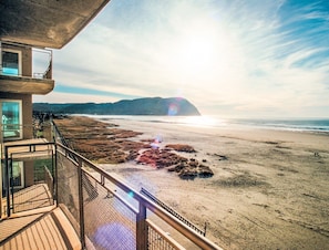 Blick auf einen Strand vom Balkon aus, mit blauem Himmel, Sandstrand und Bergen in der Ferne.